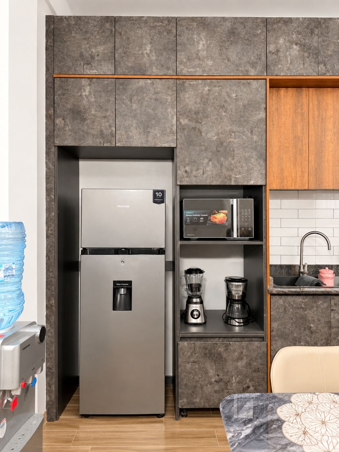 A compact kitchen with a stainless steel refrigerator, a water dispenser, a blender, and a coffee maker.