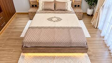 A bedroom with a large bed, wooden headboard, bedside tables, and a potted plant.