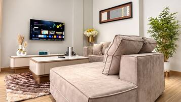 A modern living room with a sectional sofa, a flat-screen TV, a small table, and a potted plant.