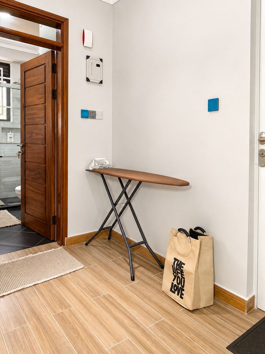 Quarto com porta de madeira, um banco, um tapete na porta e uma bolsa com a inscrição 'THE BEST YOU LOVE'.
