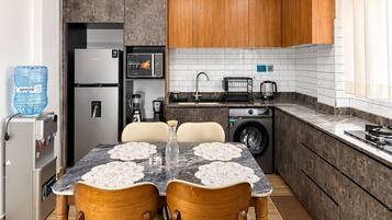 A modern kitchen with a dining area, featuring a refrigerator, microwave, sink, and a water dispenser.