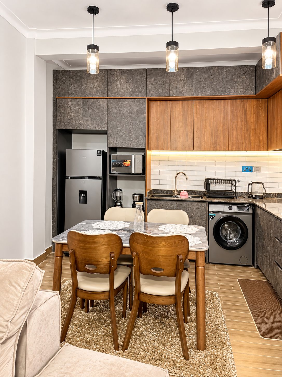 A compact kitchen with a dining area, equipped with a refrigerator, microwave, washing machine, and a coffee machine.