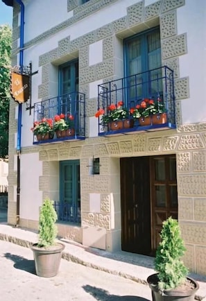 A building with a patterned facade, a balcony with red flowers, and a door with a window above it.