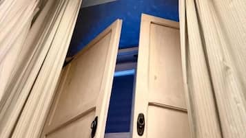 A corridor with wooden doors and curtains, leading to a room with a blue carpet.