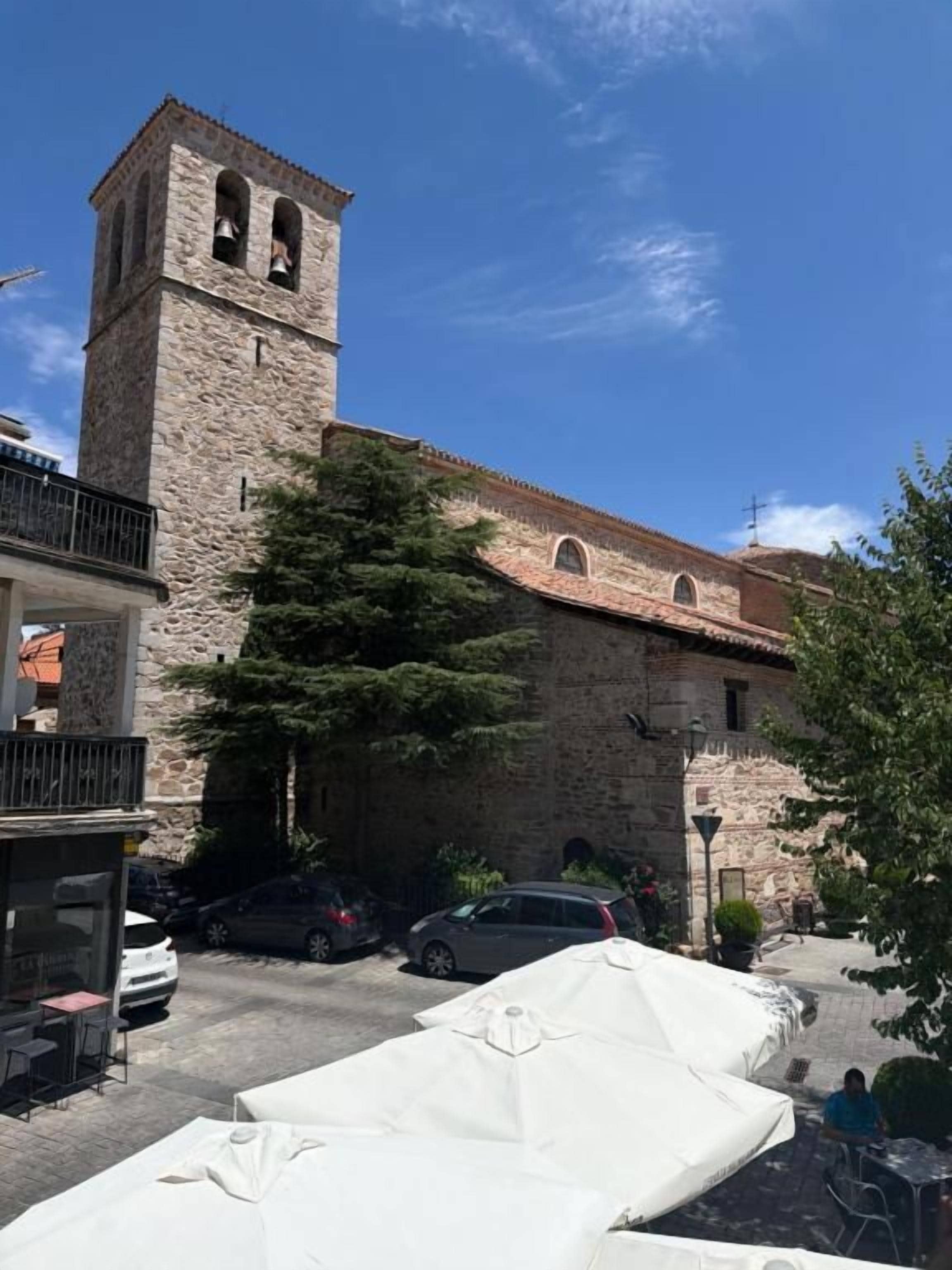 A stone building with a bell tower, outdoor seating, and parked cars.