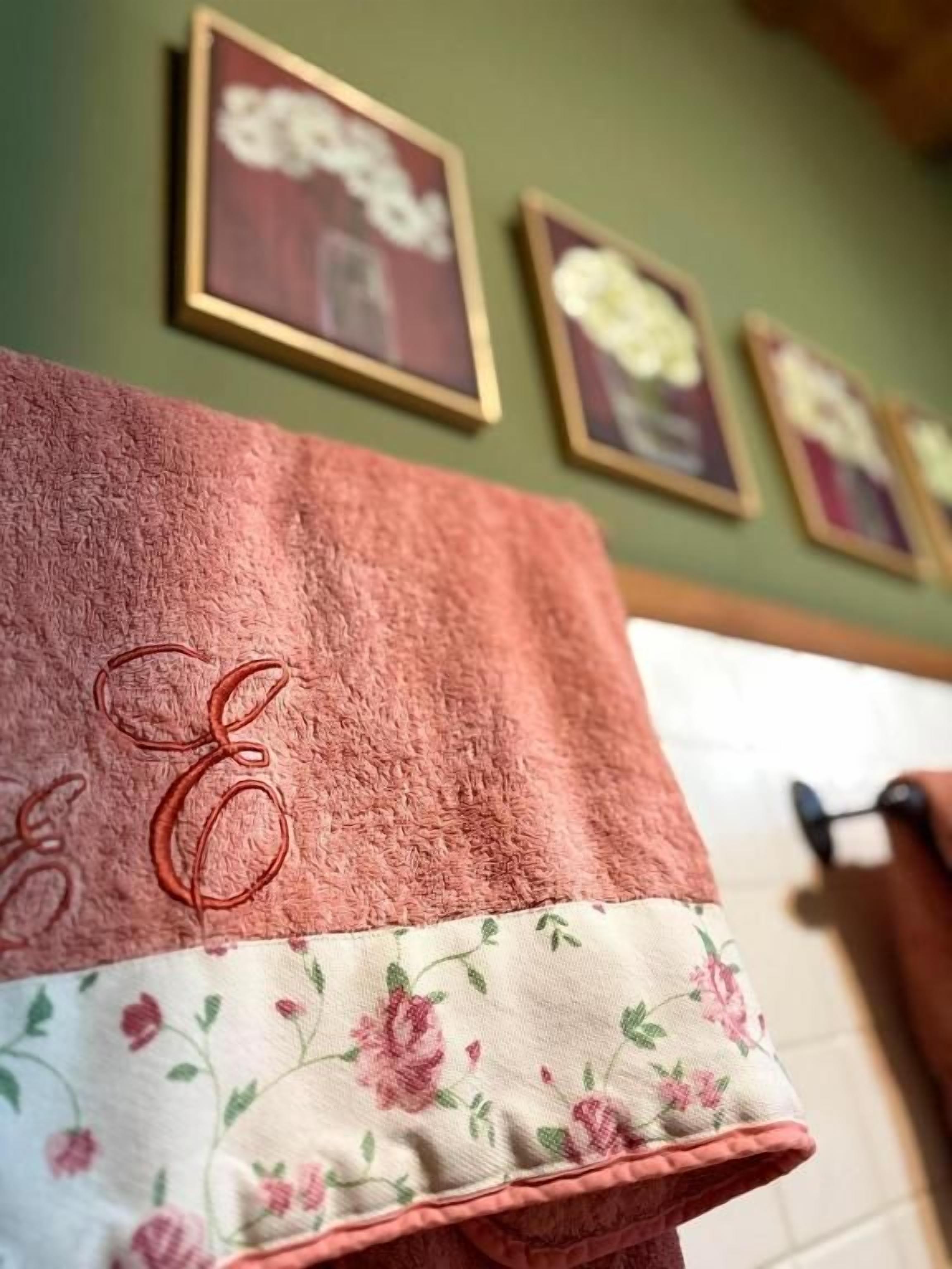 Une salle de bain avec une serviette suspendue à un porte-serviettes, un mur vert et des tableaux encadrés au-dessus.