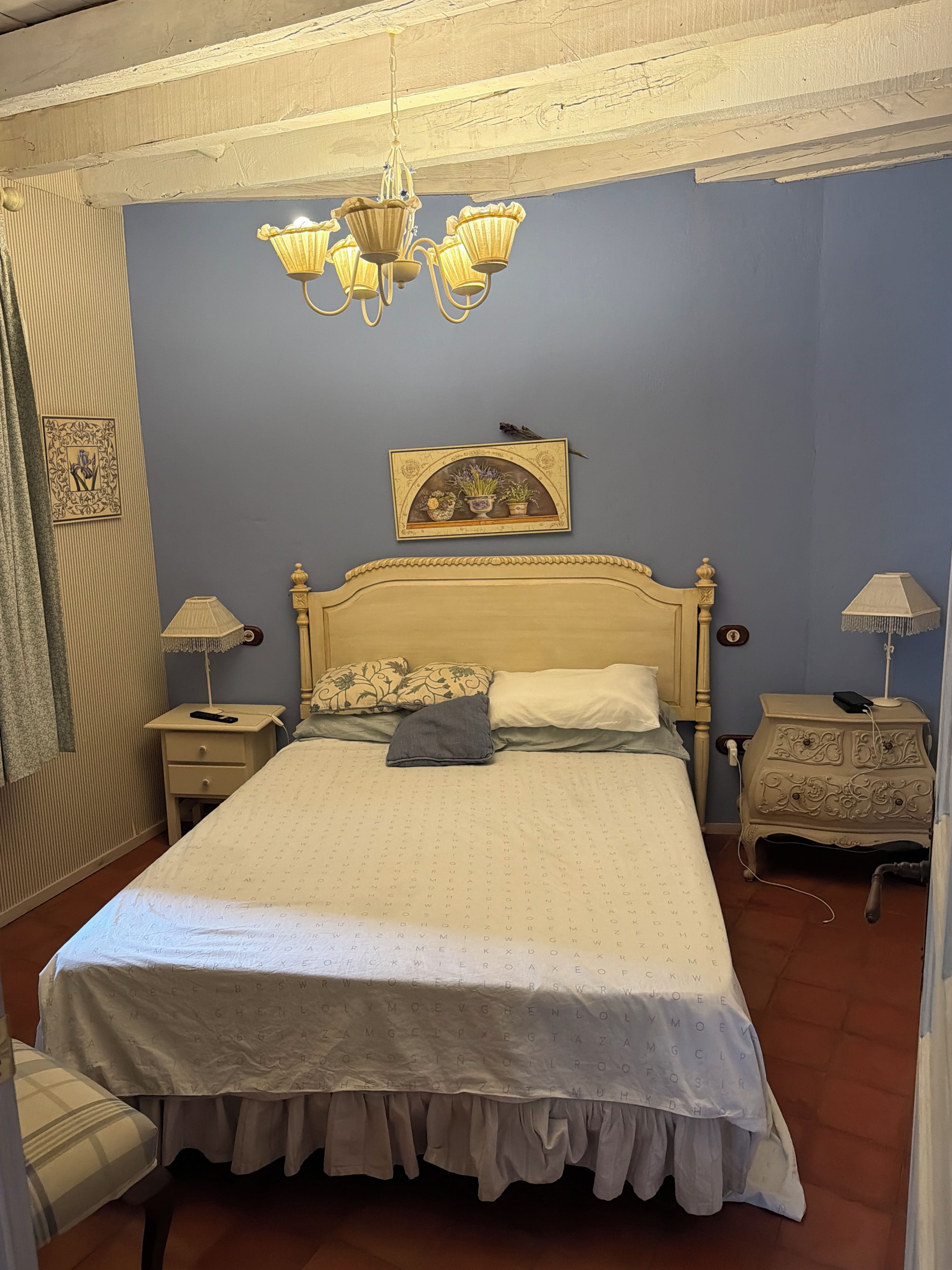 A bedroom with a bed, nightstands, a dresser, a chandelier, and a wall-mounted picture.