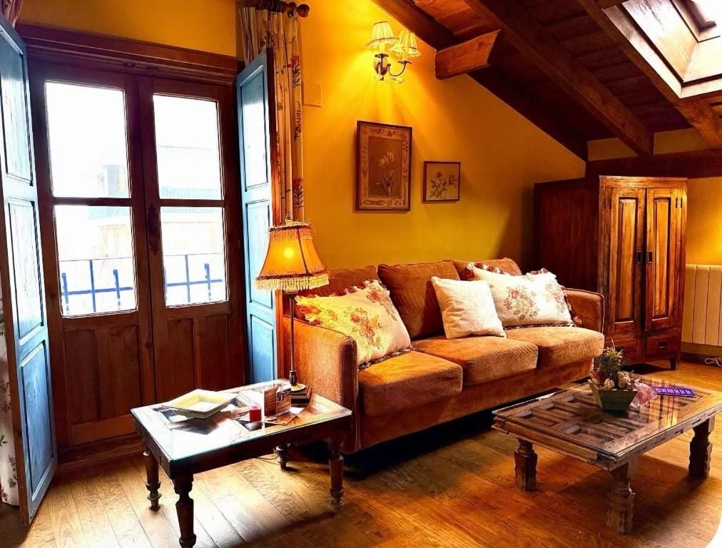 Una sala de estar acogedora con un sofá, una mesa de centro y una lámpara. Hay una ventana con cortinas y una puerta con marco de madera.