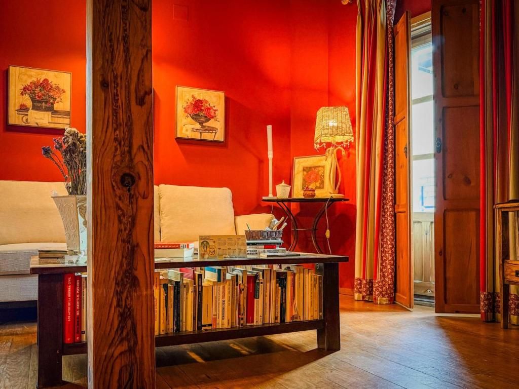 A room with a red wall, a white sofa, a wooden coffee table with books, and a lamp.