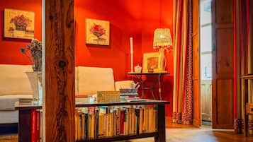 A room with a red wall, a white sofa, a wooden coffee table with books, and a lamp.