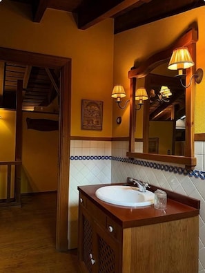 A bathroom with a wooden vanity, a white sink, and a mirror with wall-mounted lamps.