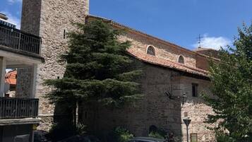Un edificio de piedra con un campanario, mesas al aire libre y coches aparcados.