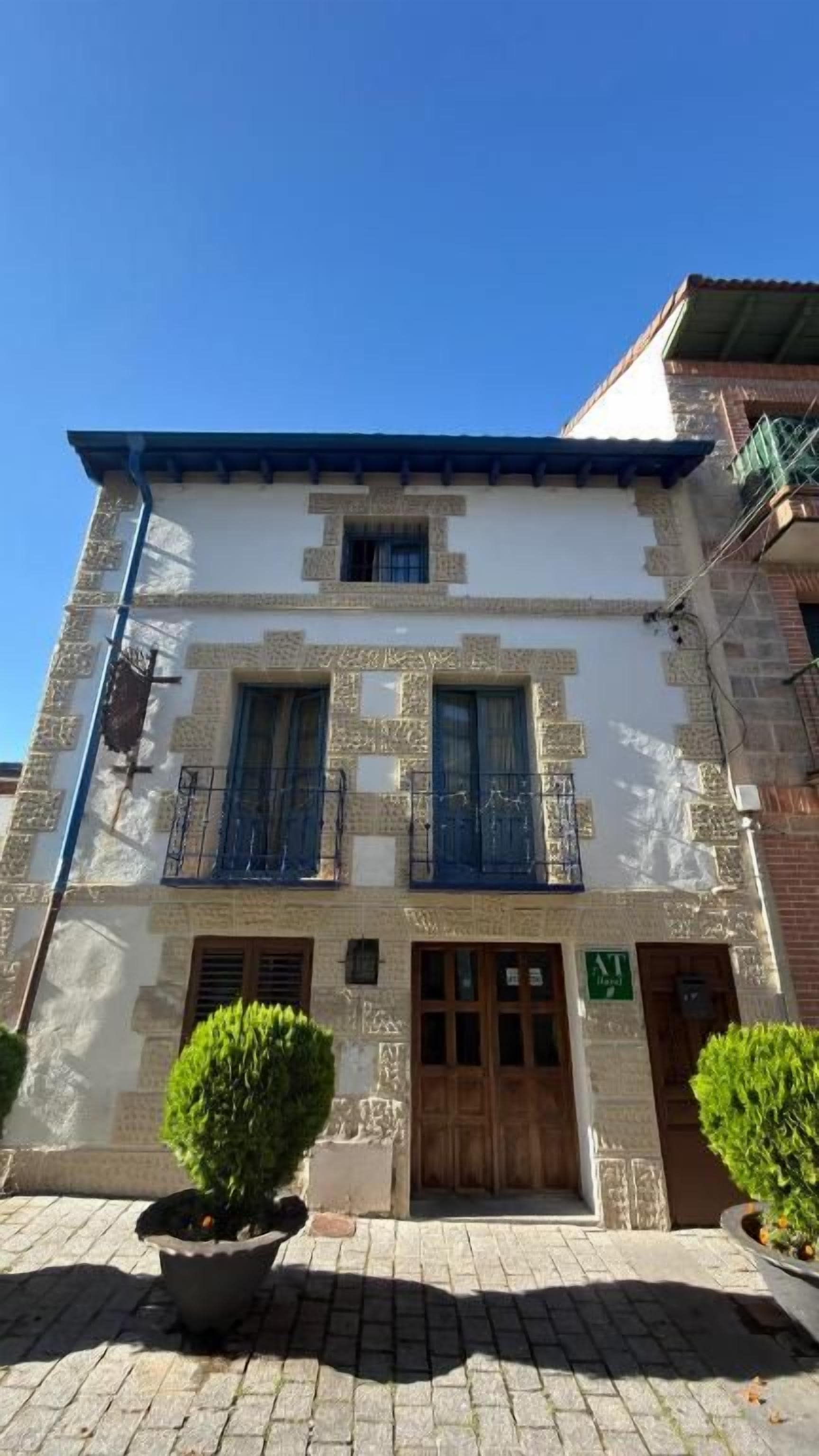 Un edificio con entrada central, dos ventanas en la planta baja y un balcón con barandillas azules.