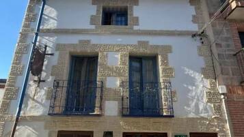 Un edificio con entrada central, dos ventanas en la planta baja y un balcón con barandillas azules.