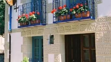 A building with a patterned facade, a balcony with red flowers, and a door with a window above it.