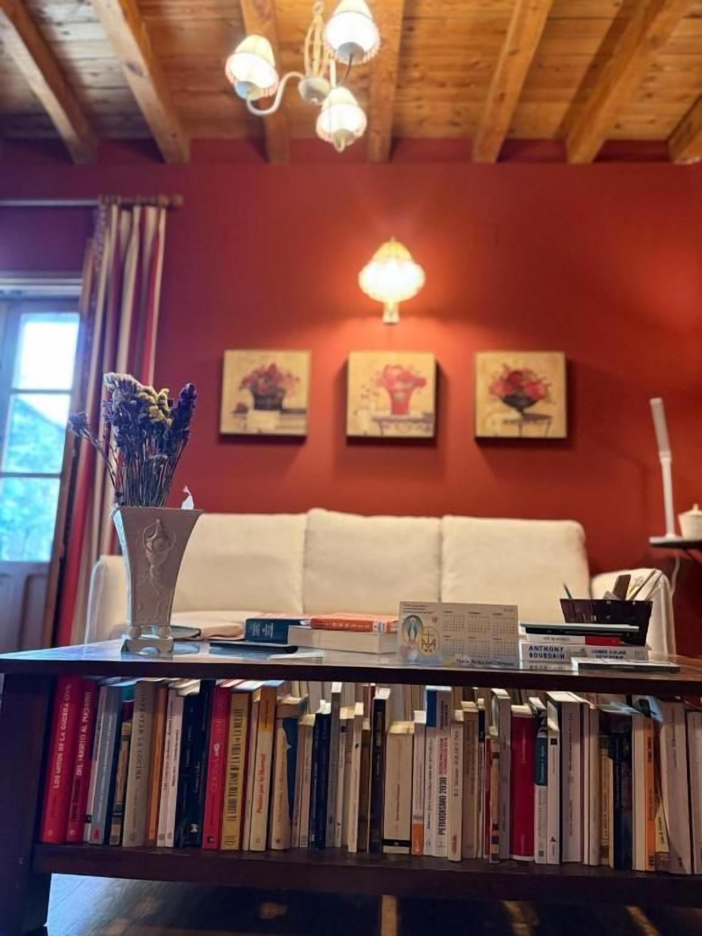 Een kamer met een boekenplank vol boeken, een vaas met gedroogde bloemen en drie ingelijste kunstwerken aan de muur.