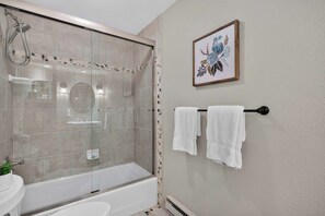 Een badkamer met een douche met glazen wand, een bad, een toilet en een handdoekrek met twee handdoeken.