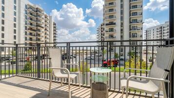 A balcony with outdoor furniture, a view of a road, and tall residential buildings.