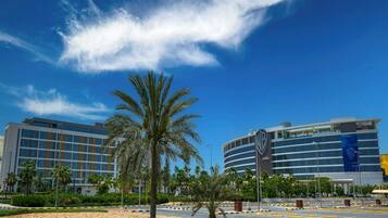 A modern hotel with a palm tree in the foreground, a clear blue sky, and a parking lot.