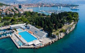 An aerial view of a coastal area with a large swimming pool, a marina, and a cityscape in the background. - Beachfront Sunshine apartment with garden in center (Split)