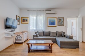 A modern living room with a sofa, a coffee table, a TV, and artwork on the walls. - Beachfront Sunshine apartment with garden in center (Split)
