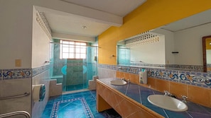 Un bany amb dues dutxes, un lavabo i una porta de vidre que dona a la zona de la dutxa.