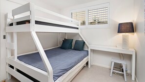 Een stapelbed met een bureau en stoel, een raam met zonwering en een lamp.