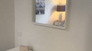 A wall-mounted mirror reflecting a lamp and a small bedside table. - Kiama Coastal Escape (Kiama)