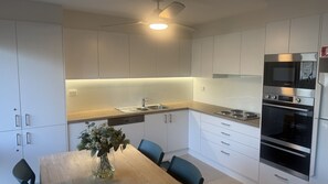 Een moderne keuken met witte kasten, een houten aanrecht, een inbouwoven en een eethoek met een tafel en stoelen.