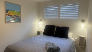 A neatly made bed with a white and gray patterned bedspread, two black pillows, and rolled towels on the side. - Kiama Coastal Escape (Kiama)