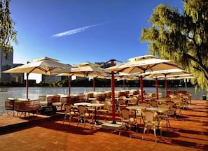 An outdoor seating area with tables and chairs under umbrellas, overlooking a body of water. - Homeinn Plus (Suzhou)