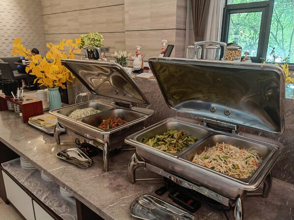 Montaje de bufé con varias estaciones de comida, incluyendo una barra de ensaladas y una estación de fideos.
