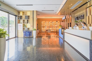 Zona de recepción de hotel con piso pulido, mostrador de recepción y área de estar con sillas y mesas.