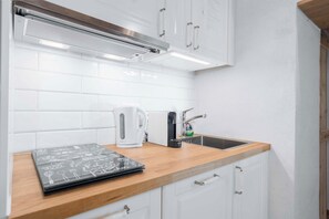 A kitchen with white cabinets, a stainless steel range hood, a kettle, a coffee maker, and a sink. - Charming house with patio near Lake Lugano (Magliaso)