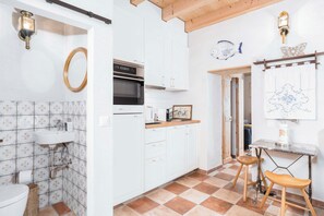 A kitchen with white cabinets, a built-in oven, and a wooden table with a chair. - Charming house with patio near Lake Lugano (Magliaso)