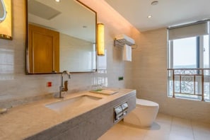 A modern bathroom with a large mirror, a sink, a toilet, and a window with a view. - Vienna International Hotel (Chongqing)