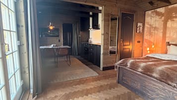 A room with a herringbone wooden floor, a bed with a dark headboard, and a large window with curtains.