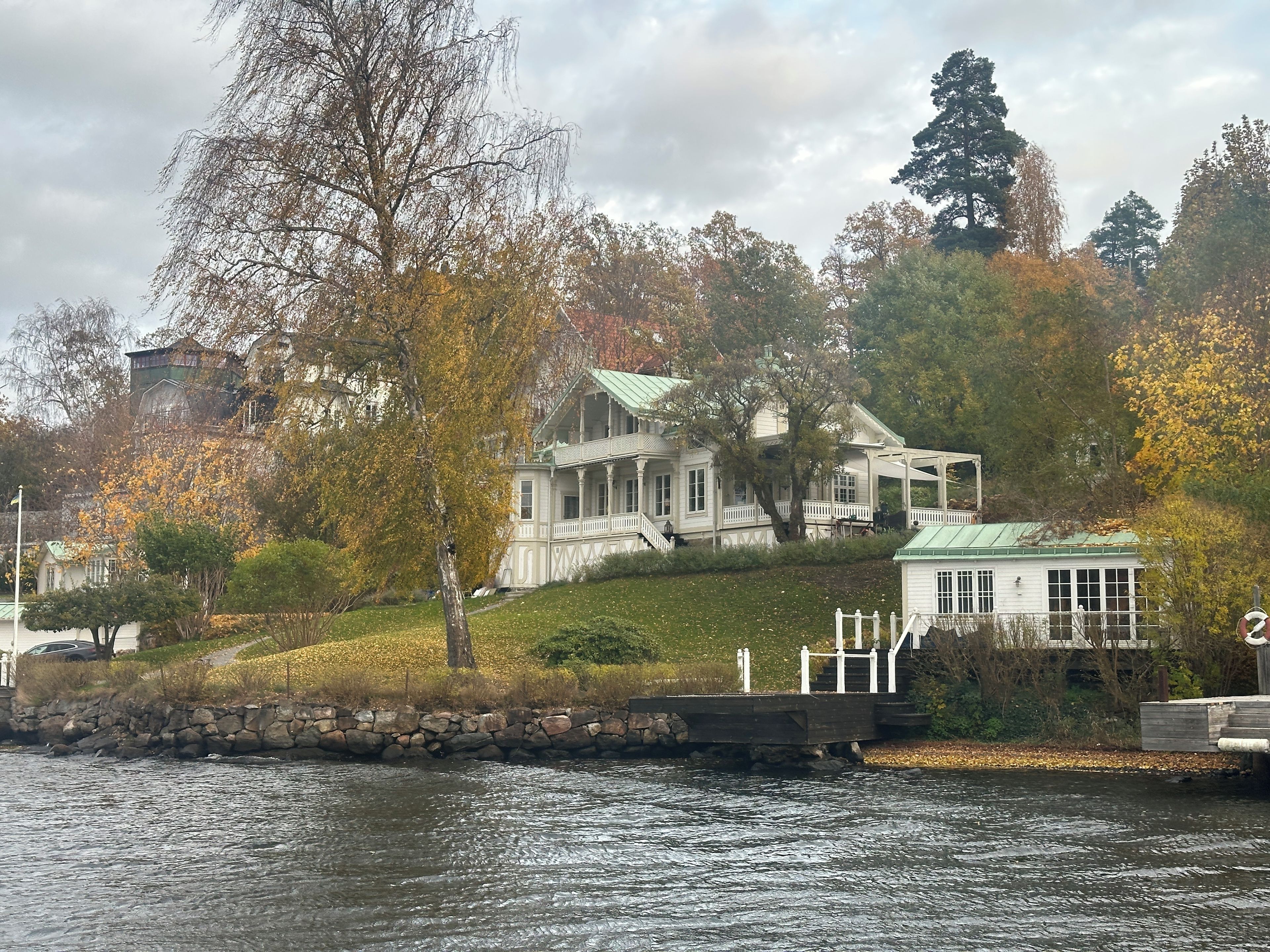 A waterfront property with a large house featuring a covered porch and a smaller building with a green roof.