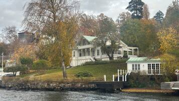 A waterfront property with a large house featuring a covered porch and a smaller building with a green roof.