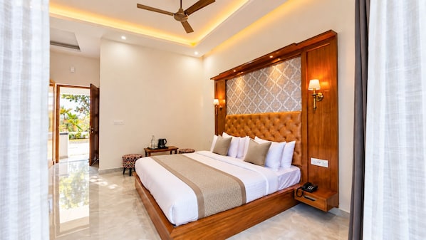 A hotel room with a large bed, a ceiling fan, a bedside table with a lamp, and a view of the outdoors.