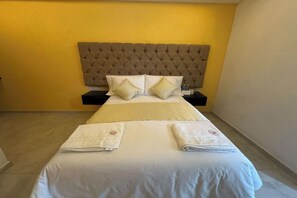 A hotel room with a tufted headboard, a bed with white linens and two pillows, a nightstand with a lamp, and a yellow wall. - OYO Hotel Familiar Tollan (San Pedro Cholula)