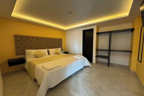 A modern bedroom with a tufted headboard, a bed with white bedding, a nightstand, a wardrobe, and a shelf unit. - OYO Hotel Familiar Tollan (San Pedro Cholula)