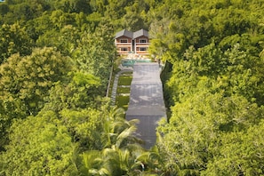 Una casa rodeada de abundante vegetación, con piscina visible y camino de entrada pavimentado.