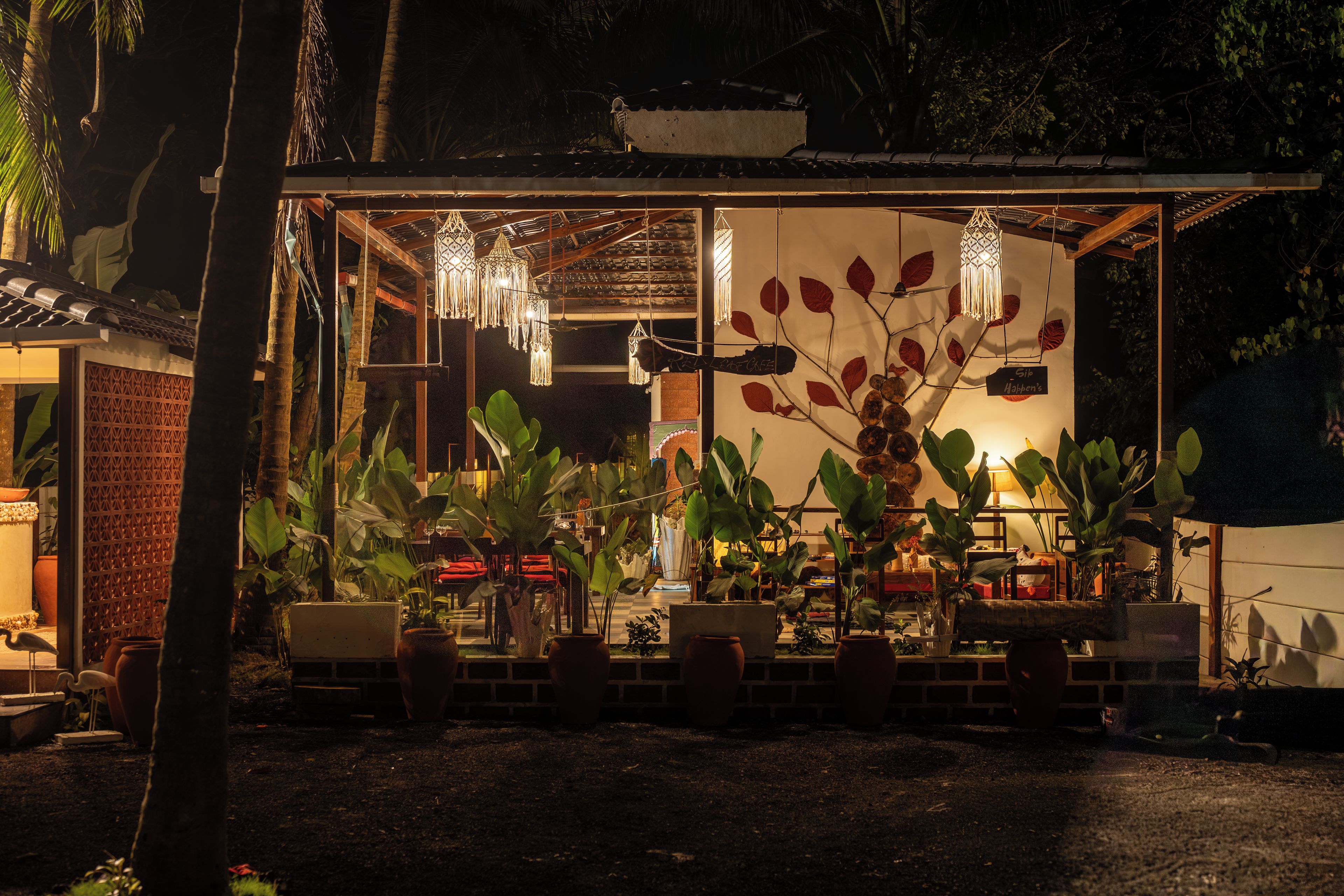Espaço ao ar livre com mesas e cadeiras, cercado por vasos de plantas e elementos decorativos.