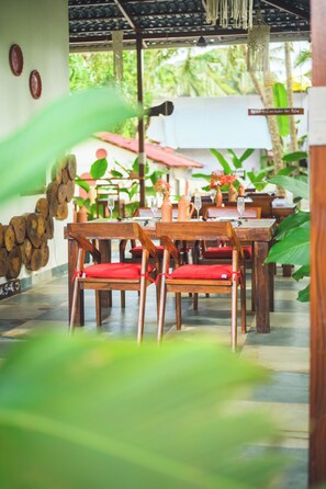 A restaurant with wooden tables and chairs, some with red cushions. - De Red Earth (Arambol)