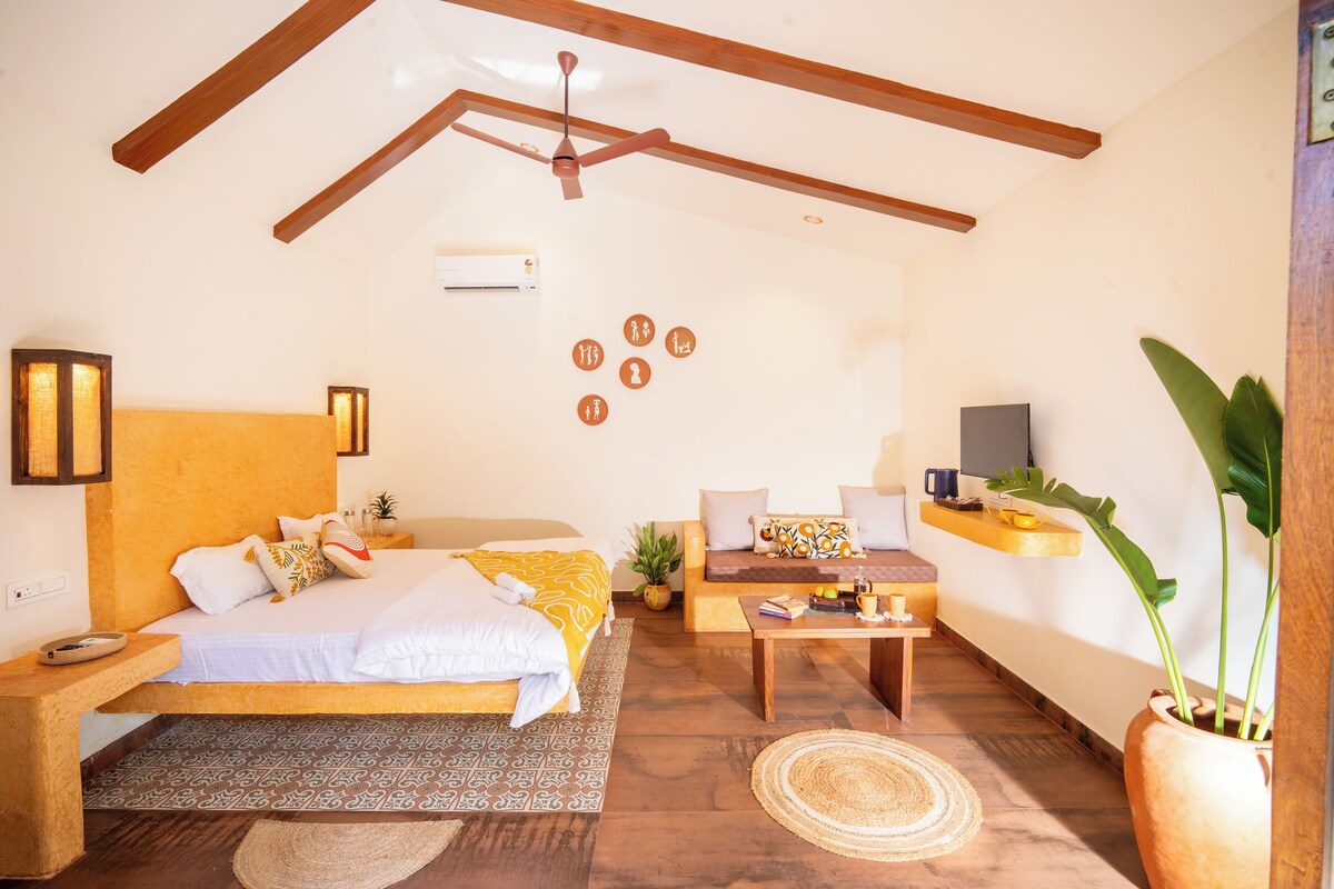 Une pièce comprenant un lit, un canapé, une table basse, un ventilateur de plafond, un téléviseur fixé au mur et une plante en pot.