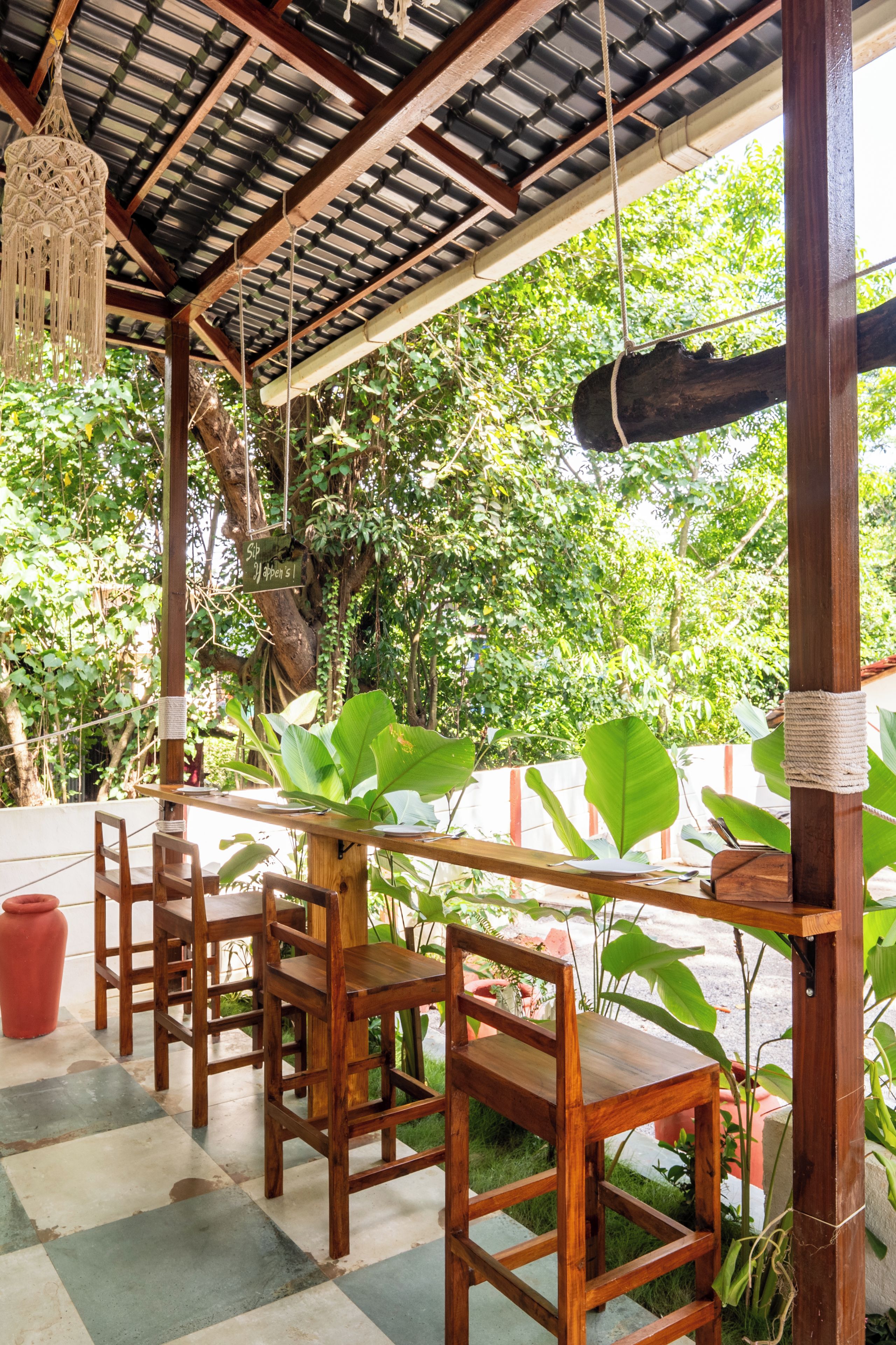 A wooden outdoor seating area with tables and chairs, surrounded by greenery and a view of trees.