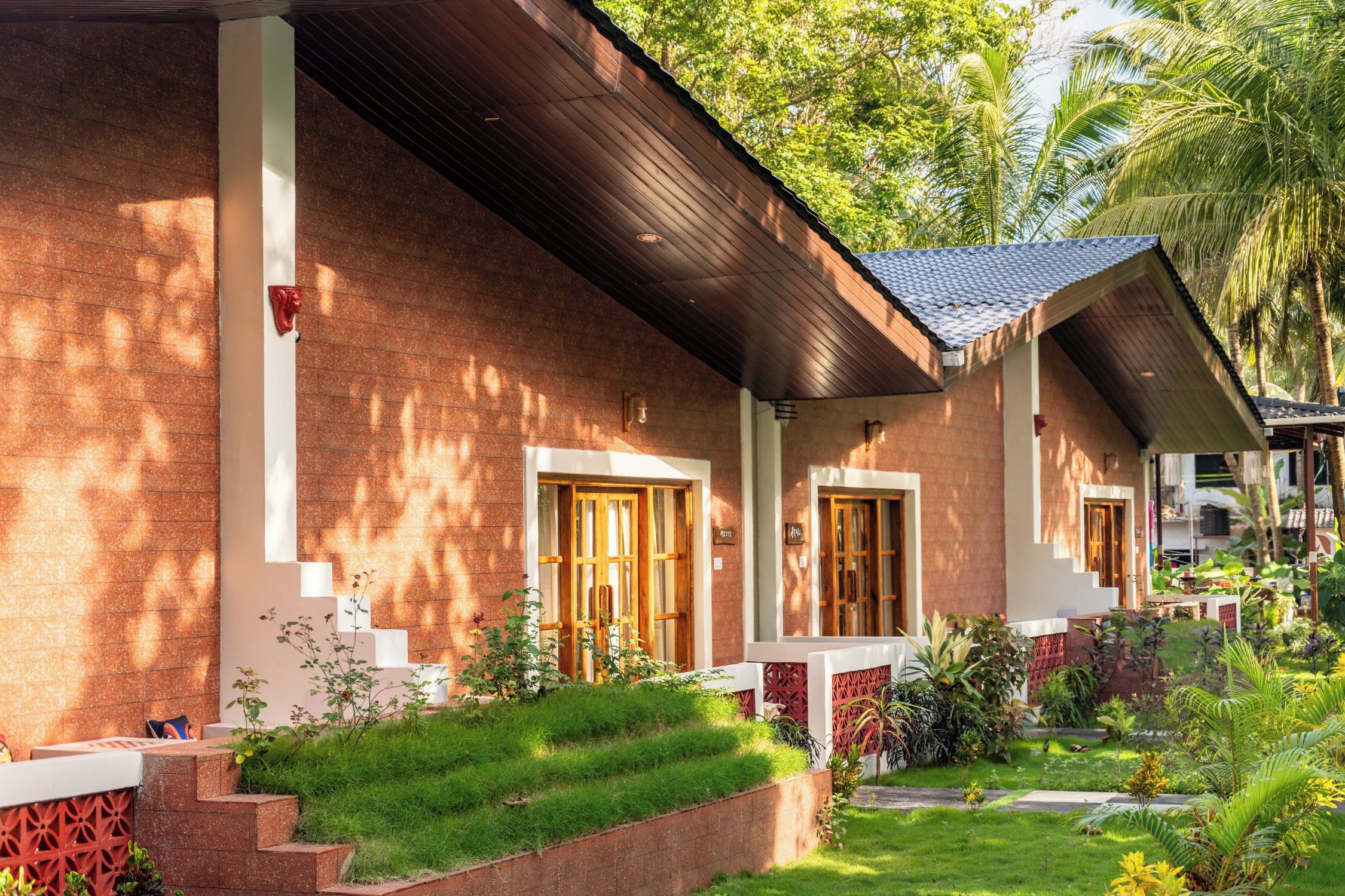 A bungalow with a sloped roof, wooden doors, and a small garden with grass and plants.