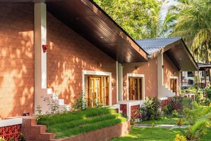 Una cabaña con techo inclinado, puertas de madera y un pequeño jardín con césped y plantas.