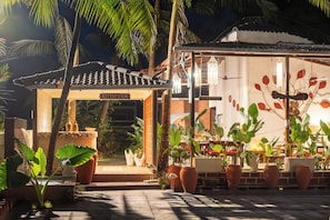 A traditional building with a tiled roof, a signboard, and a pathway leading to a covered area with potted plants. - De Red Earth (Arambol)